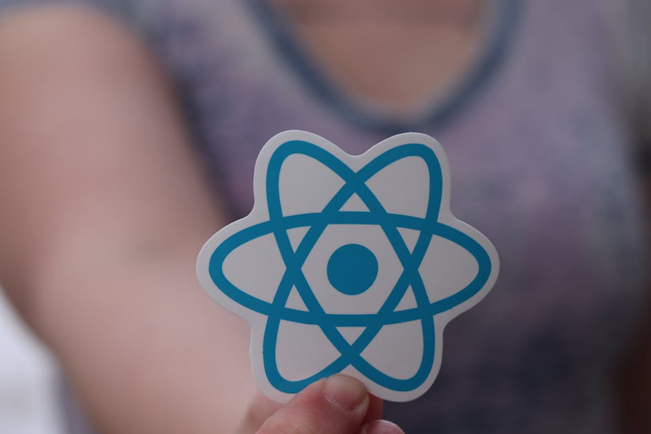 A person holding a sticker shaped like an atom symbol with blue and white colors in front of their chest. The background appears to be a room with a wooden floor and a glass table, illuminated by natu